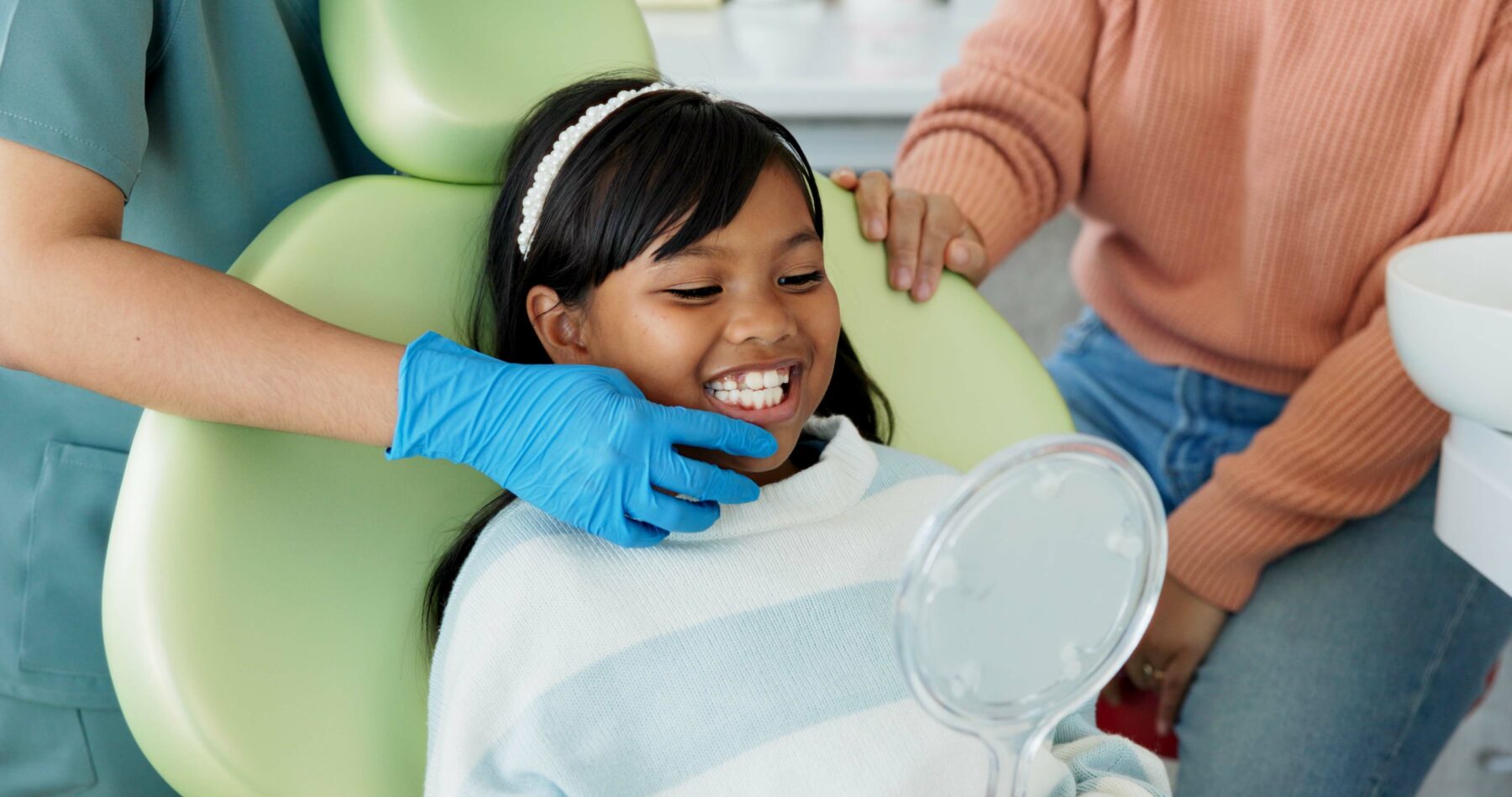 Child smiles as a dentist holds up a mirror for her to see her teeth.